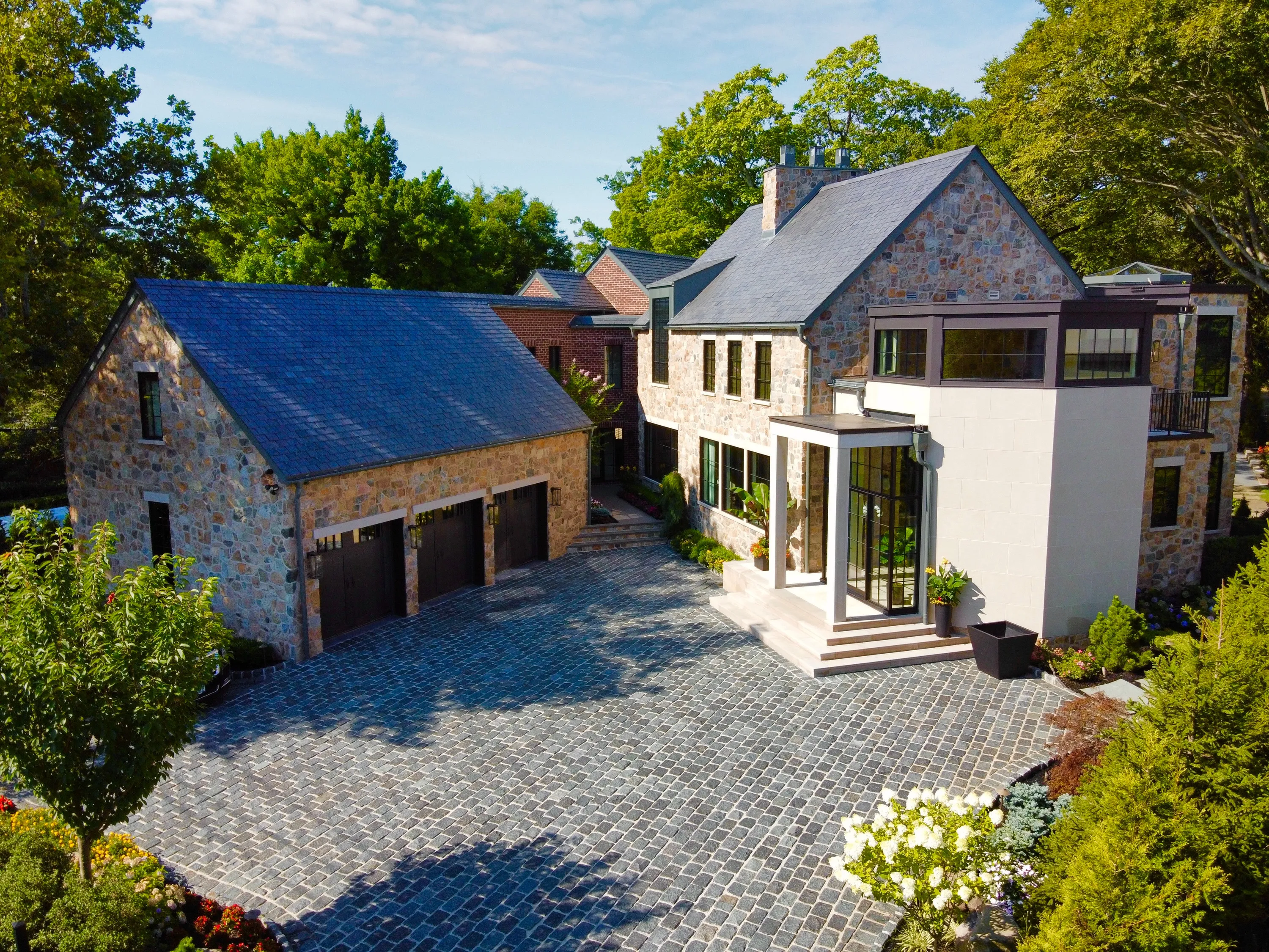 Aerial view of a stone residence, detached garage, and landscaped motor court in New York.