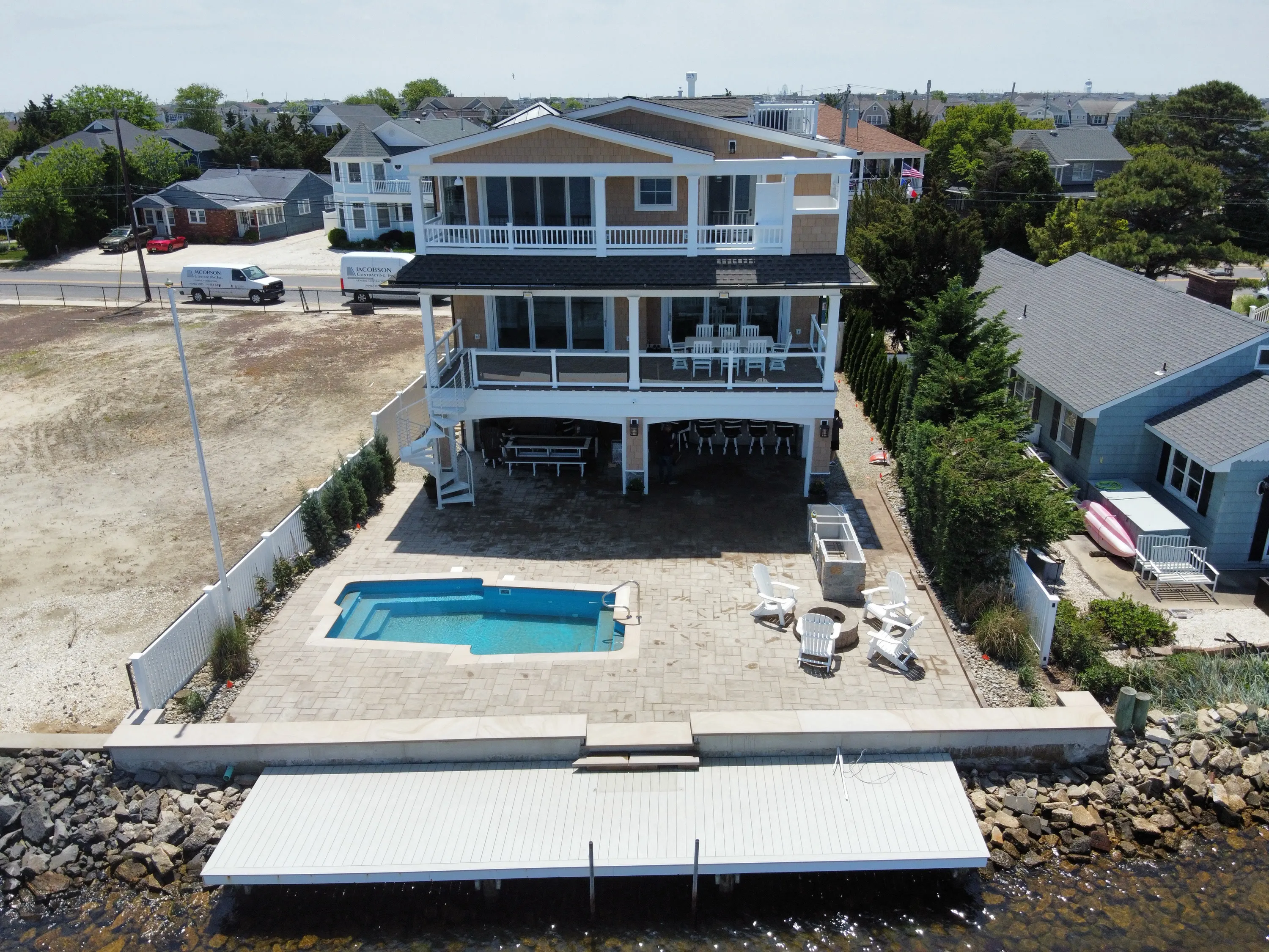 Aerial rear view of a coastal residence, pool terrace, and waterfront edge.