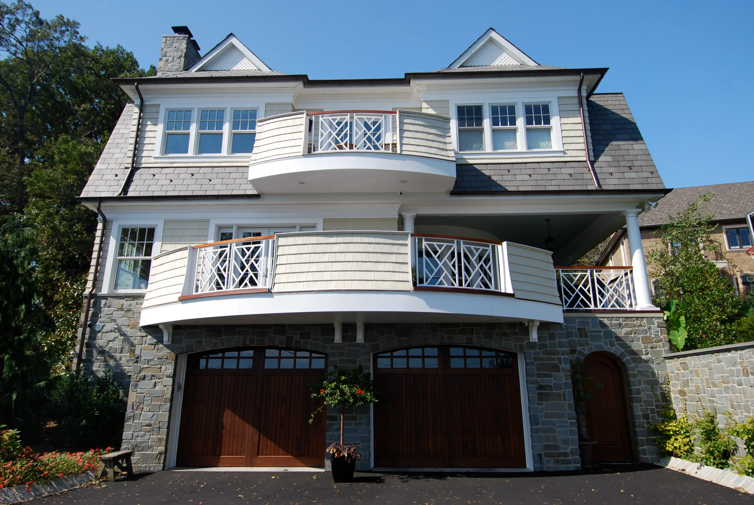 Rear elevation with curved balconies, stonework, and wood garage doors.