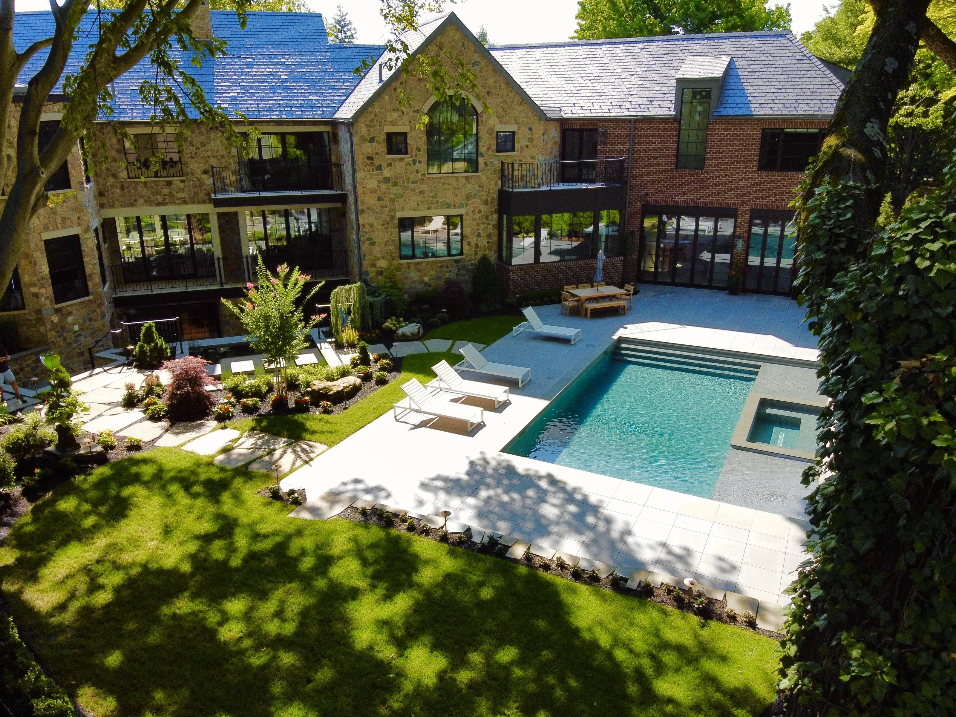 Aerial view of a stone and brick residence surrounding a landscaped rear lawn and pool.