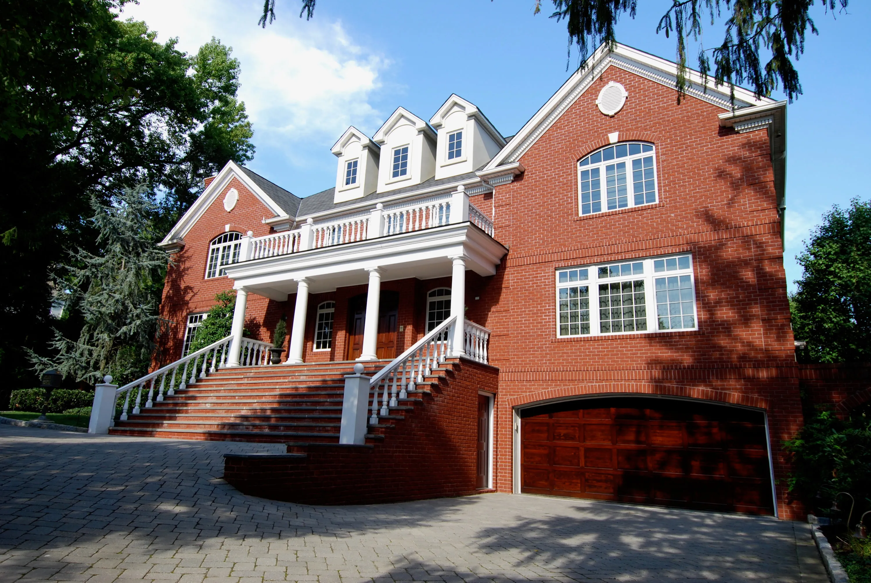 Front three-quarter view of a red brick residence with a columned entry and stepped terraces.