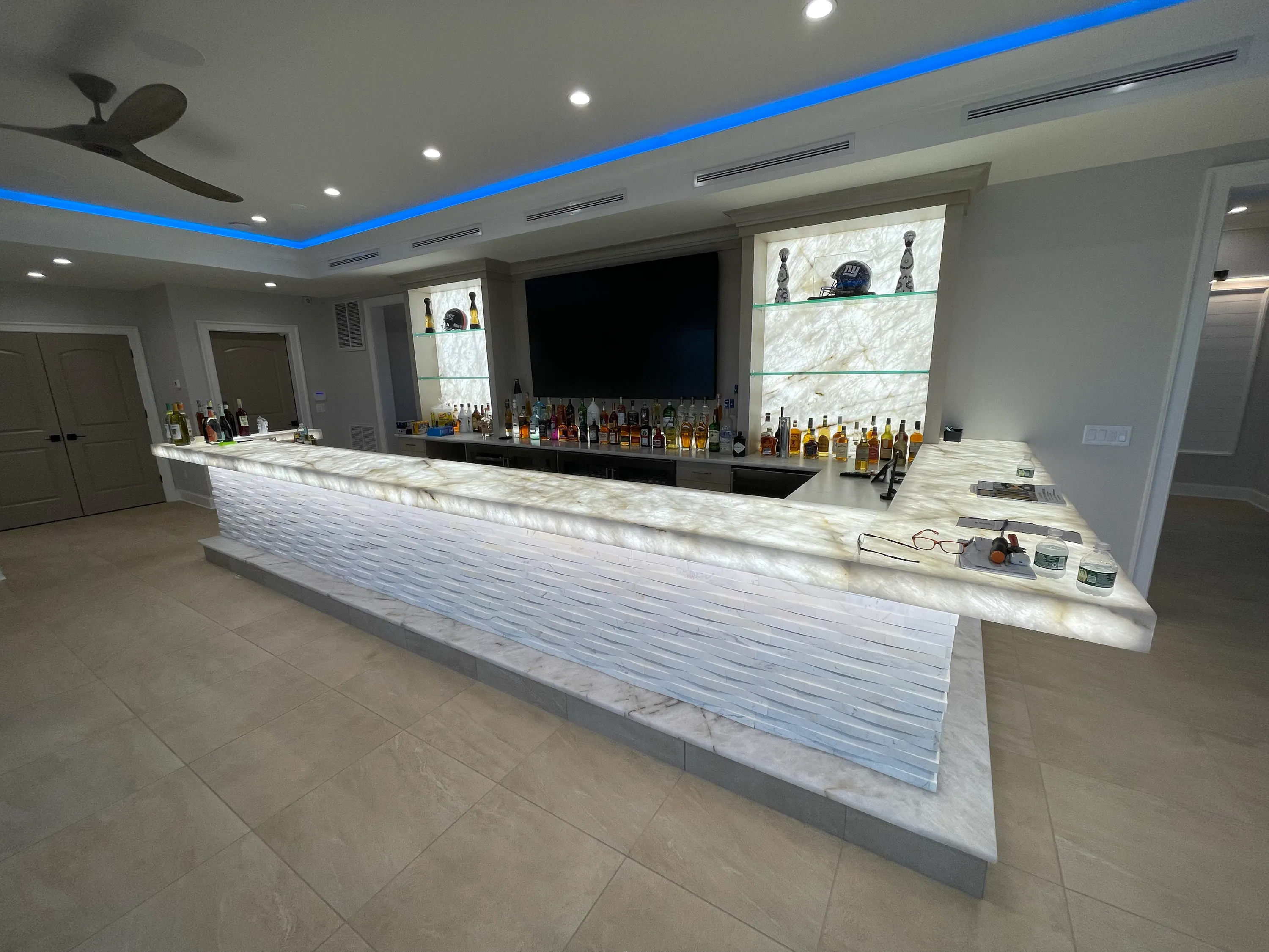 Custom bar with an illuminated stone front, display cabinetry, and generous counter space.