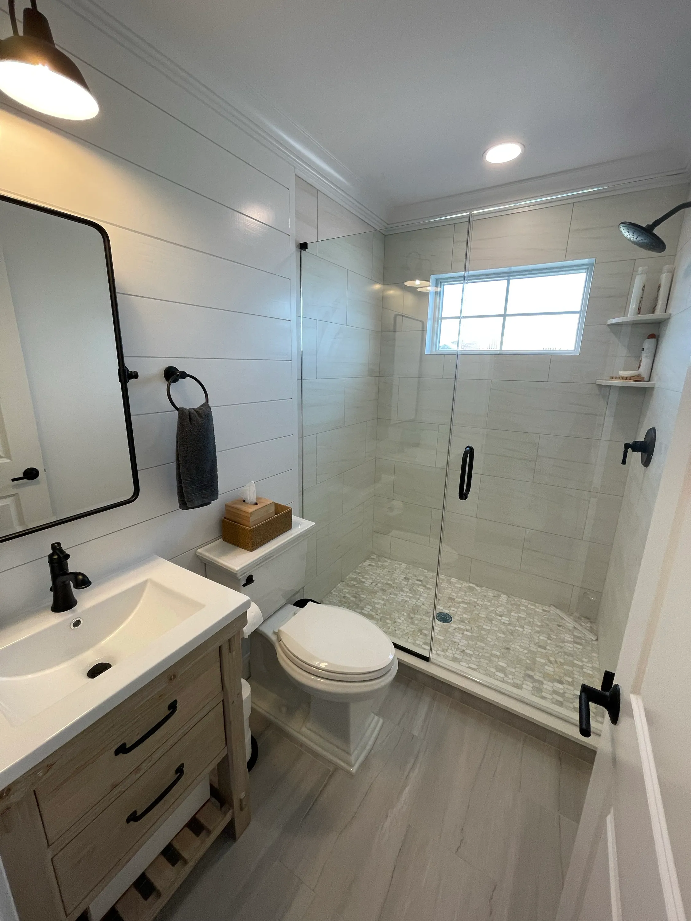 Bathroom with a glass shower, white tile, and black fixtures.