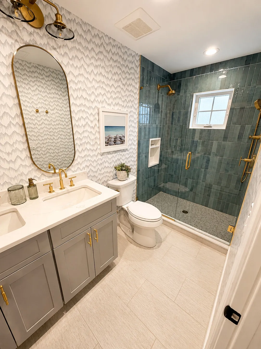 Bathroom with teal shower tile, brass fittings, and patterned wall covering.