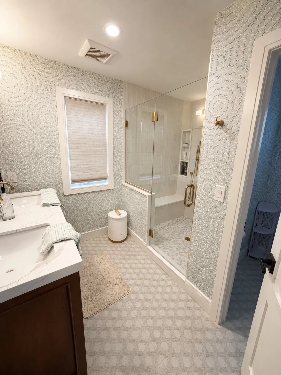 Bathroom with pale patterned walls, dark cabinetry, and a glass shower.