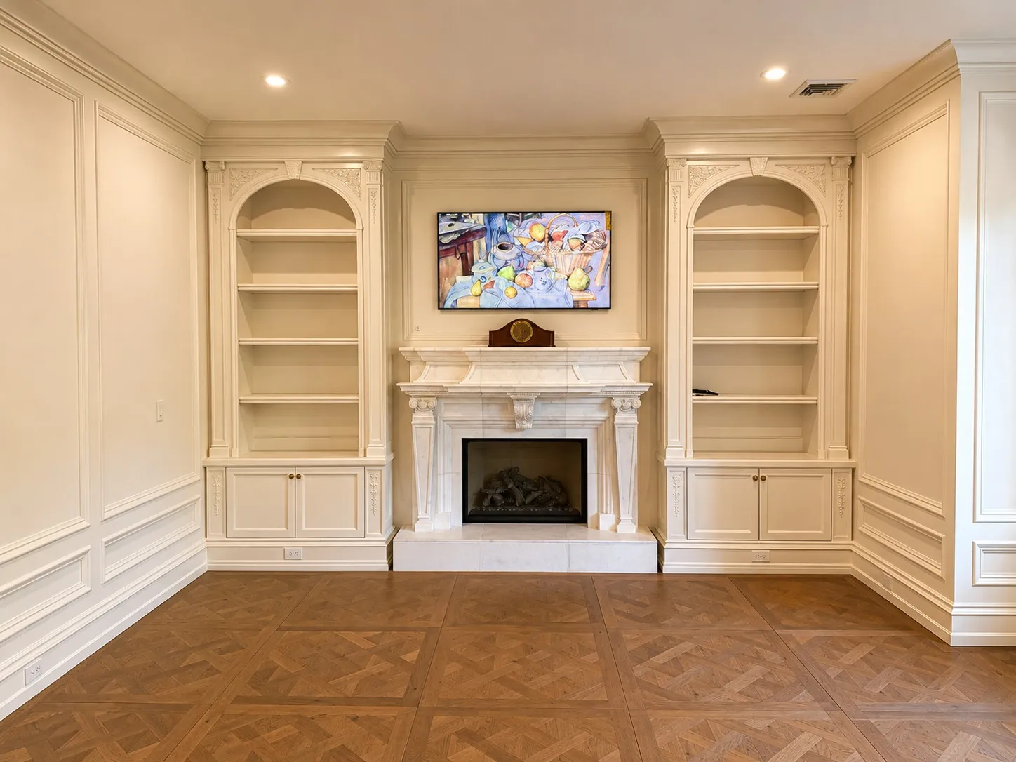Paneled room with built-in shelving, a stone fireplace, and parquet flooring.