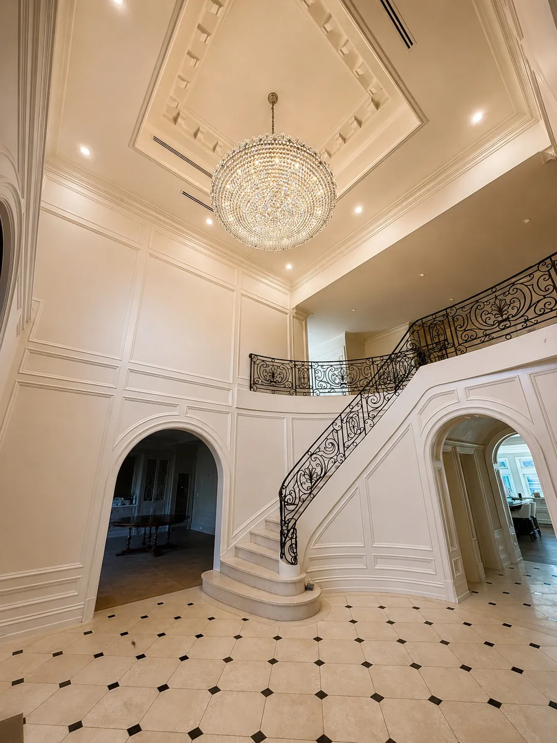 Double-height foyer with a curved stair, decorative railing, and chandelier.