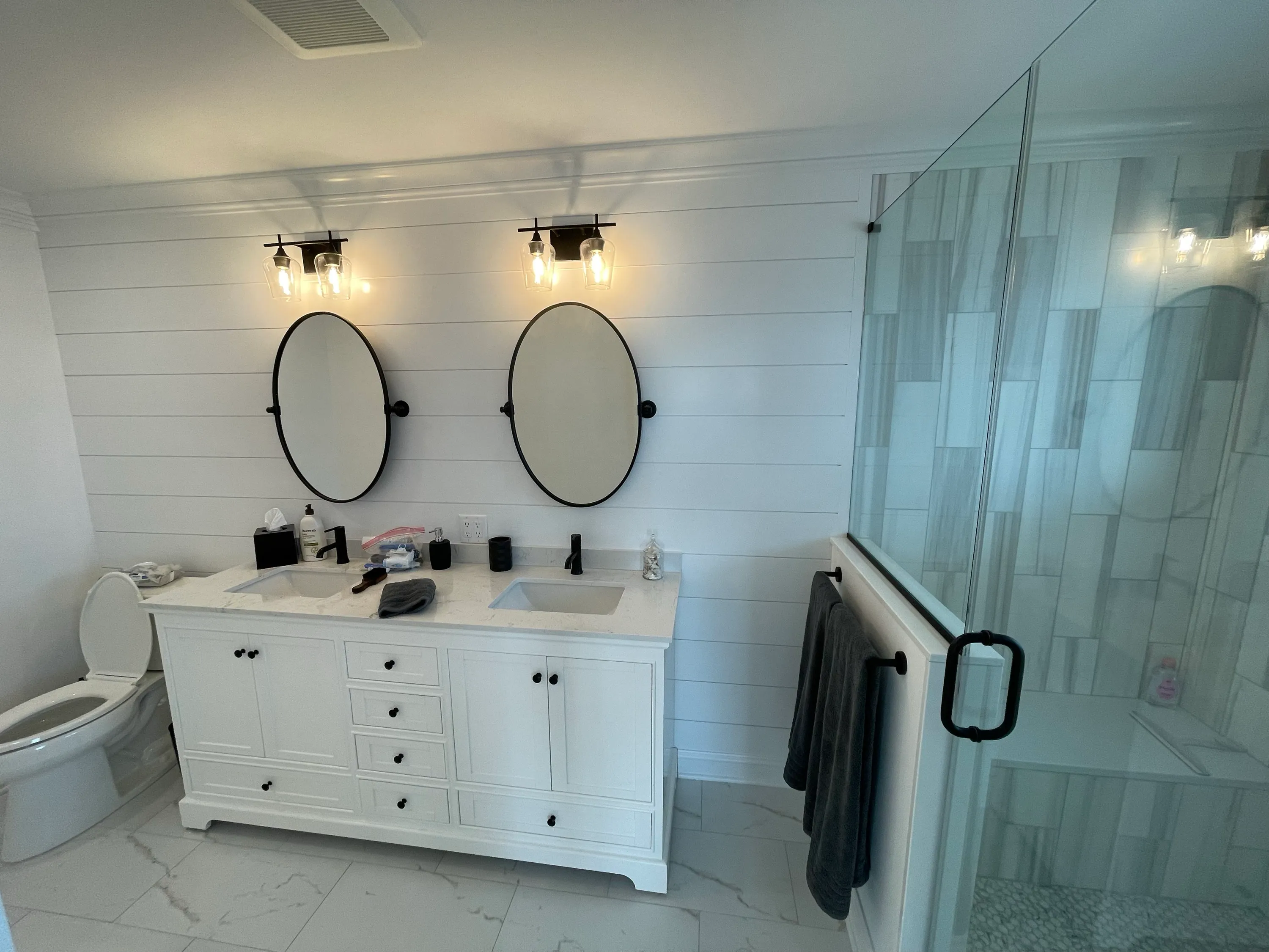 Primary bathroom with twin vanities, shiplap walls, and a glass shower.