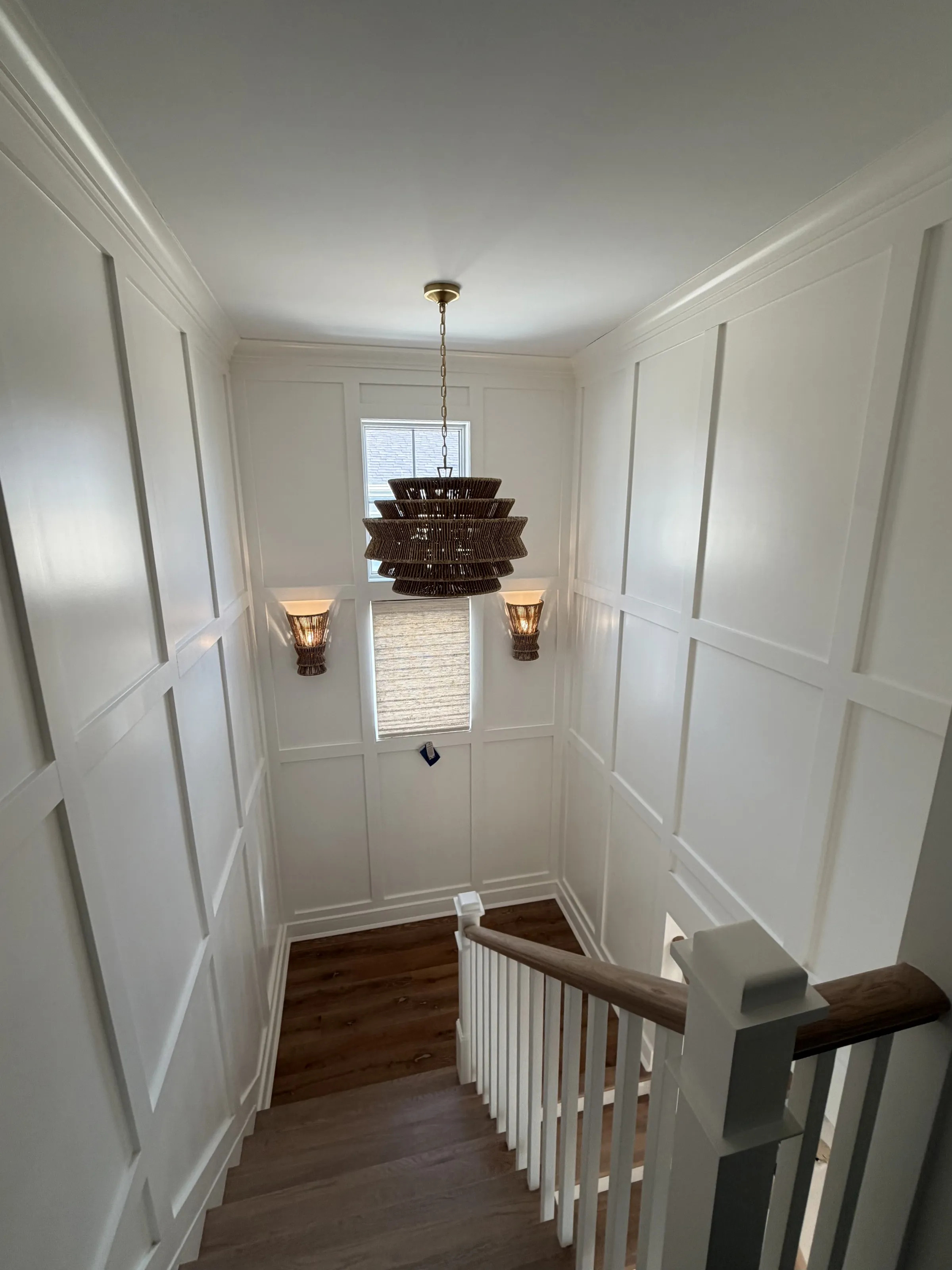 Paneled stair hall with wood treads and a woven pendant light.