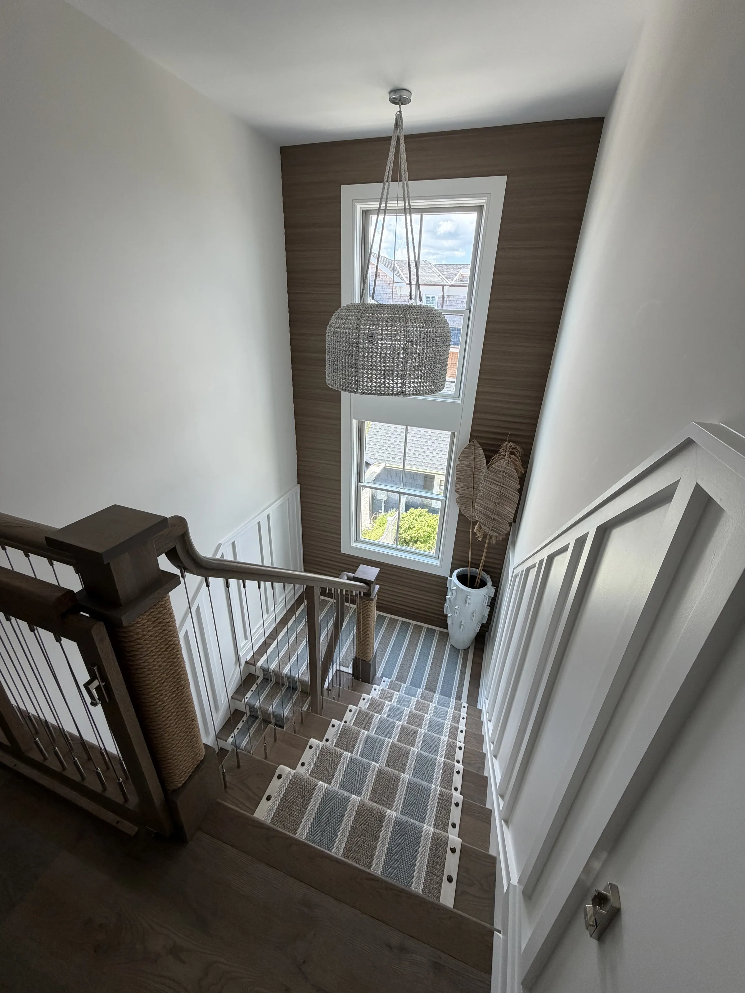 Tall stair hall with cable railing, wood treads, and a large pendant light.