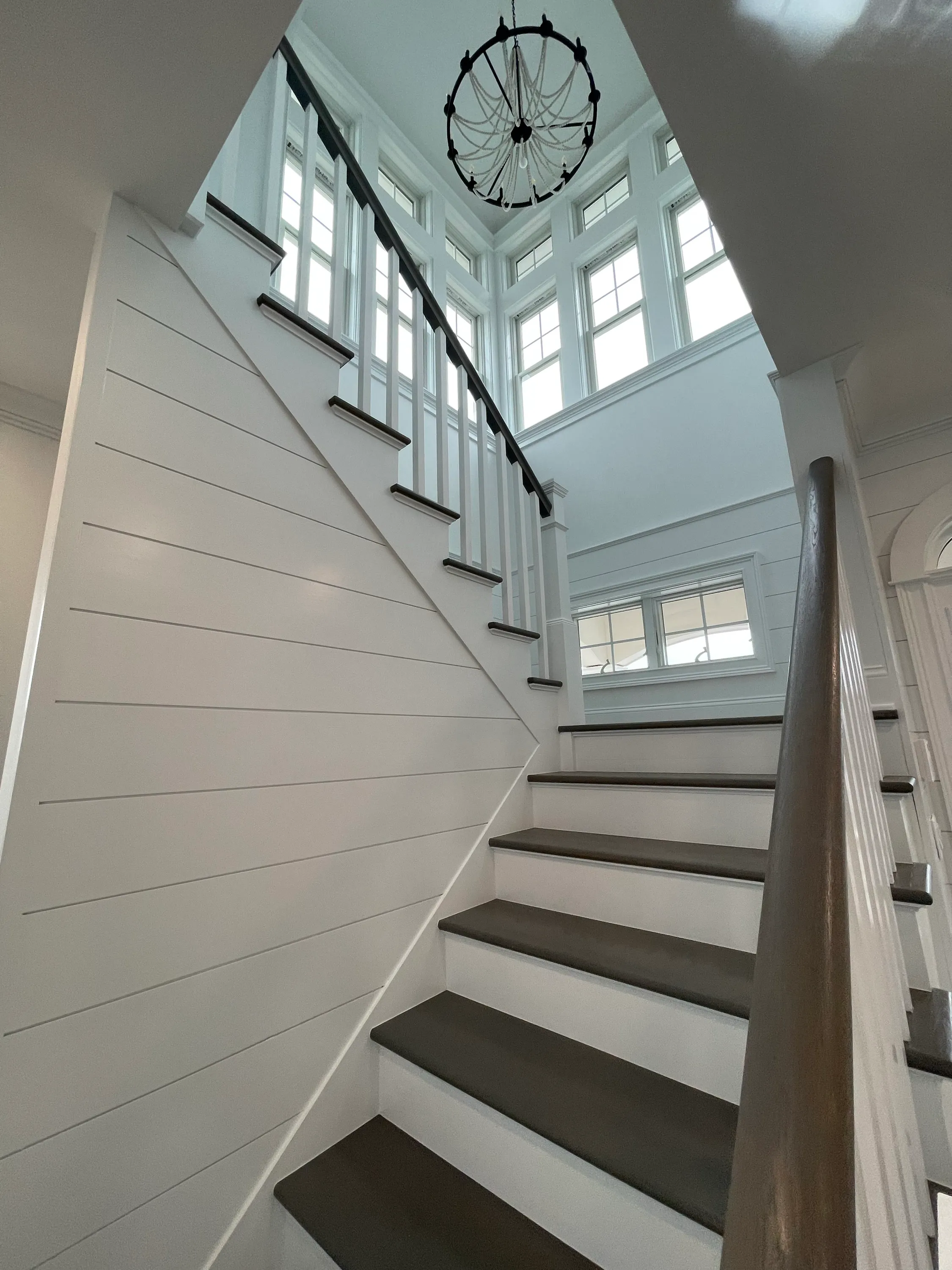 White stair with wood treads, shiplap walls, and tall windows.