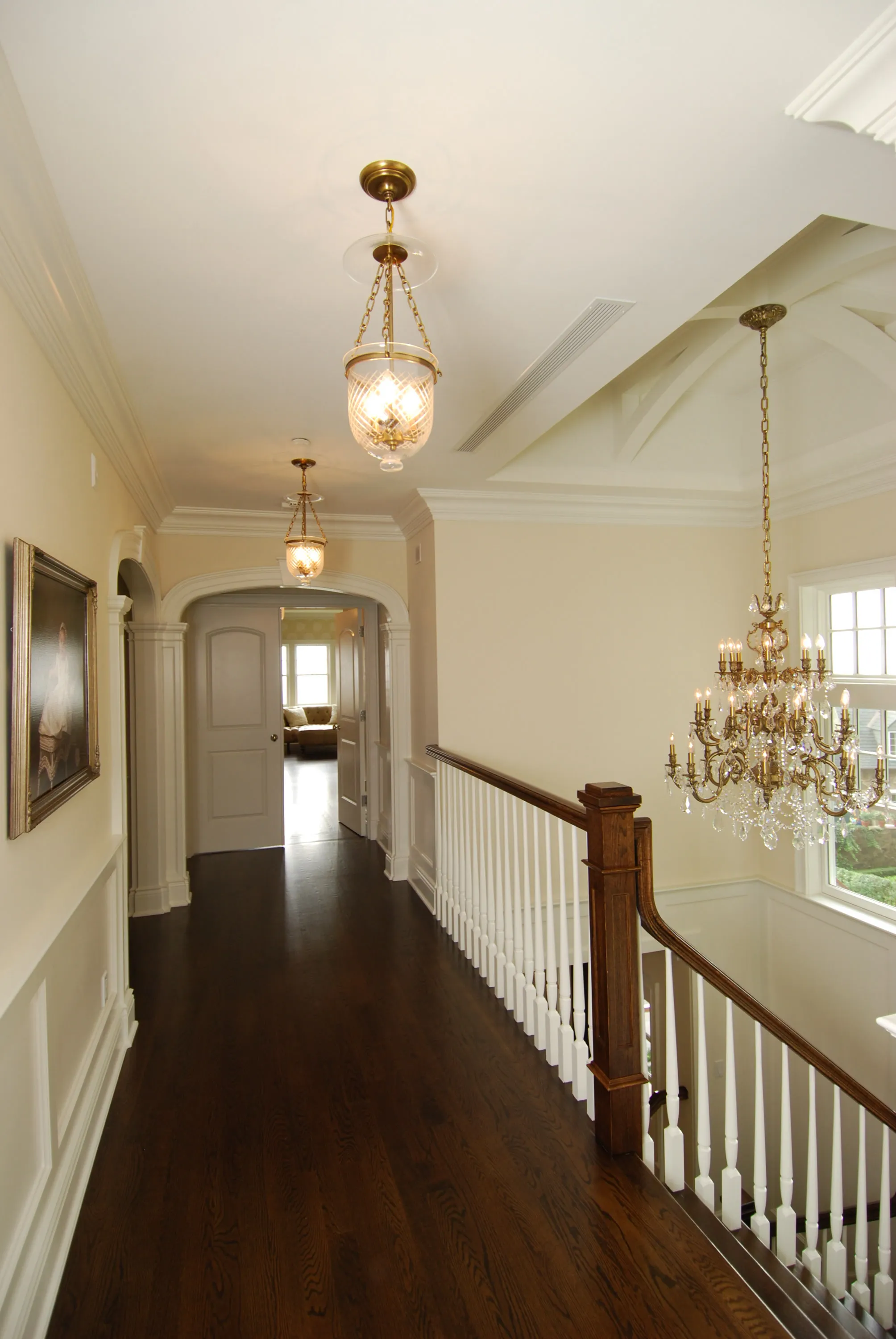 Upper hall with dark wood flooring, detailed trim, and chandelier lighting.