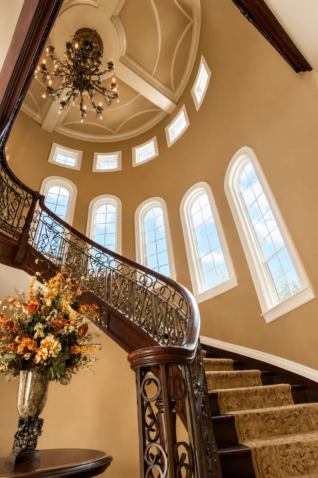 Ornamental curved staircase rising through a tall windowed hall.
