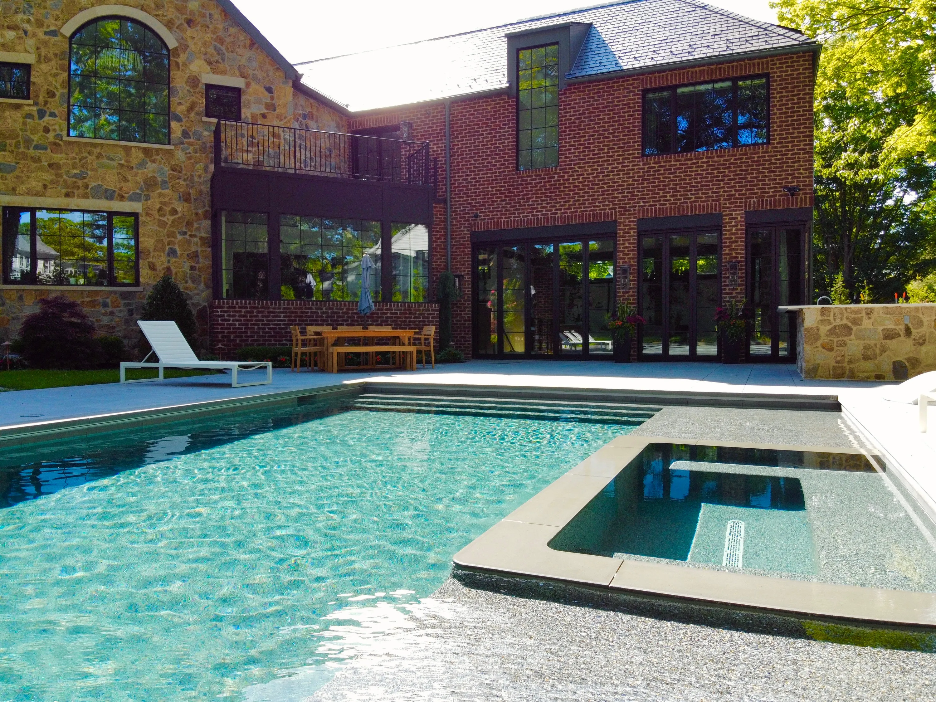 Pool terrace and integrated spa beside a brick residence in New York.